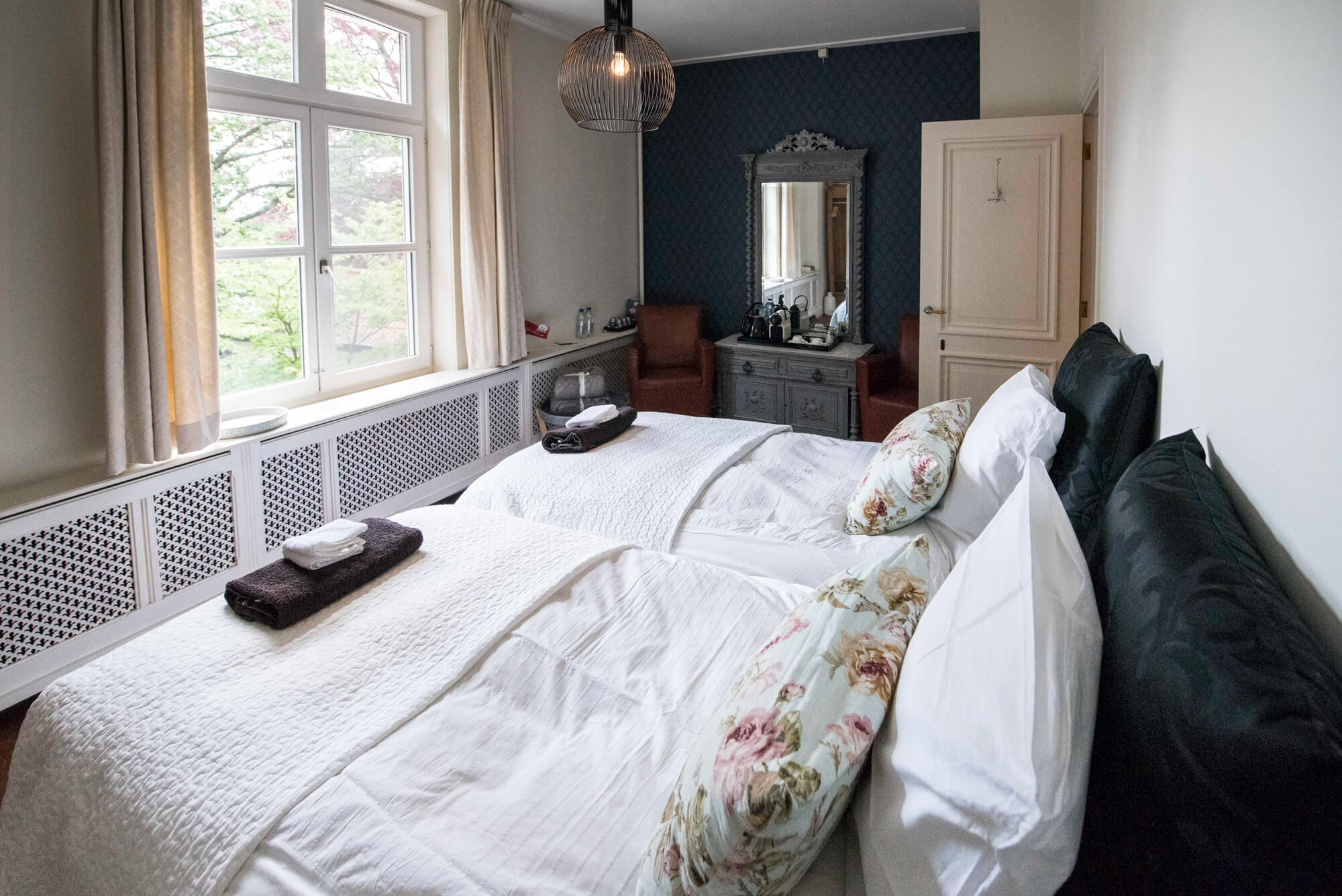 Zijlade met een spiegel en een vaas met bloemen met een weerspiegeling van het bed in de spiegel.