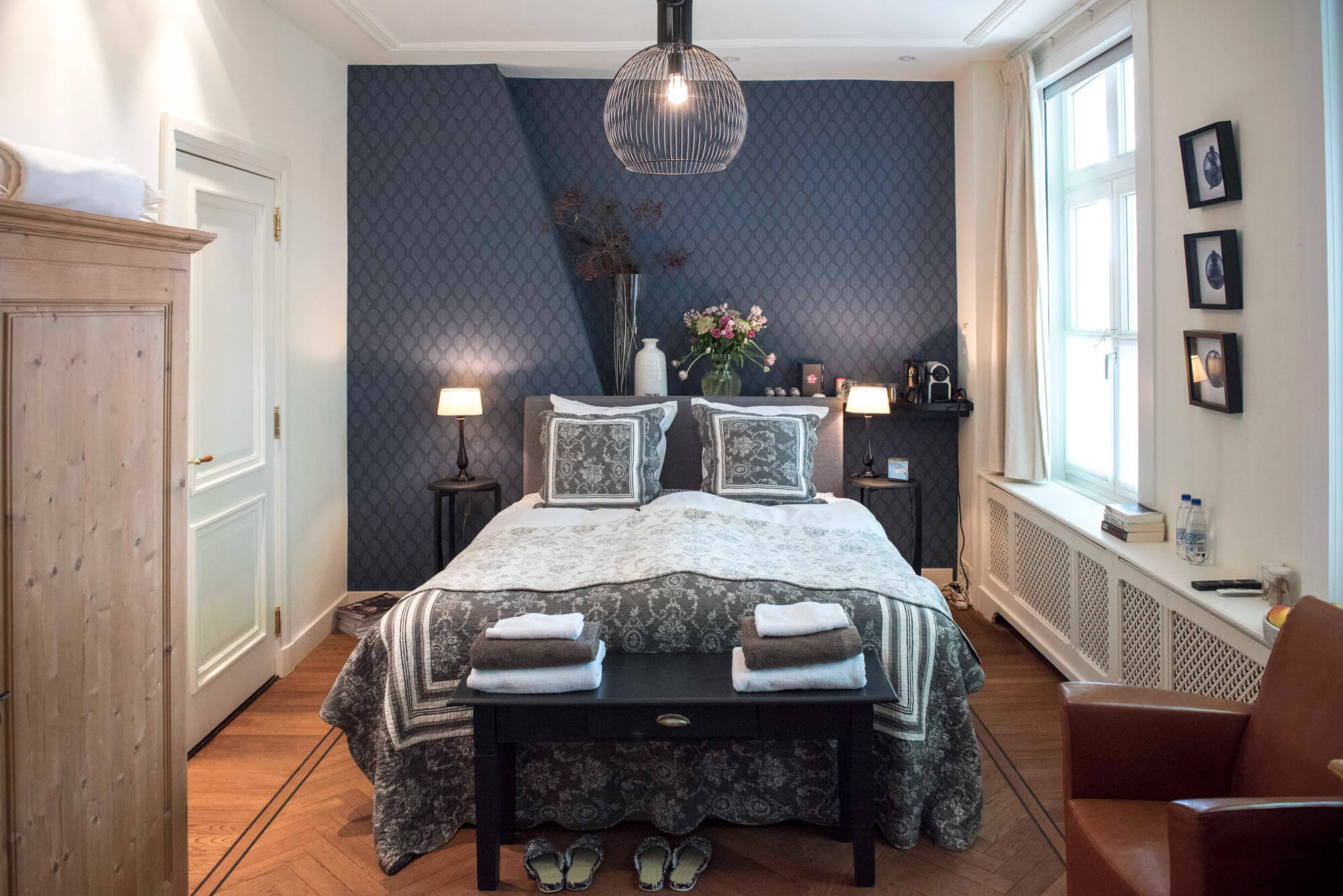 Zijlade met een spiegel en een vaas met bloemen met een weerspiegeling van het bed in de spiegel.